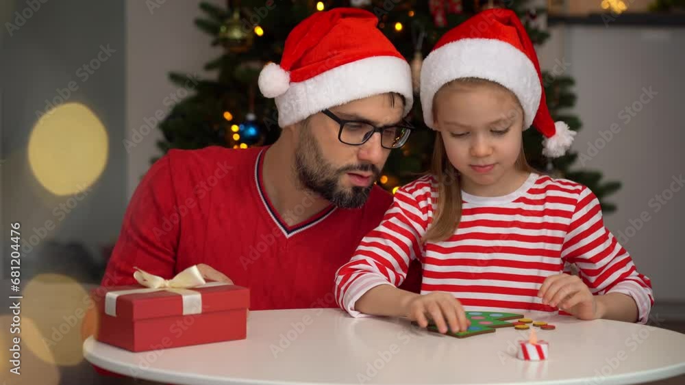 Happy family, father and little daughter fun play collecting wooden puzzle in form of Christmas tree. Leisure for holidays with child. Christmas