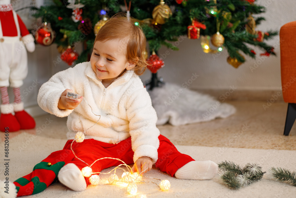 Adorable little girl having fun on a soft carpet in front of a Christmas tree