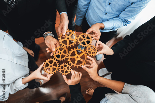 Group of multiracial business people joining gear wheels together as effective unity and productive teamwork concept. Efficient system business team process for solution solving. Meticulous photo
