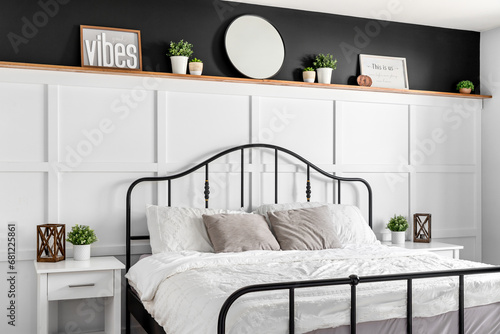 A farmhouse bedroom detail shot with wainscoting, decorations on a natural wood shelf with black paint above, and a black metal bed frame. 