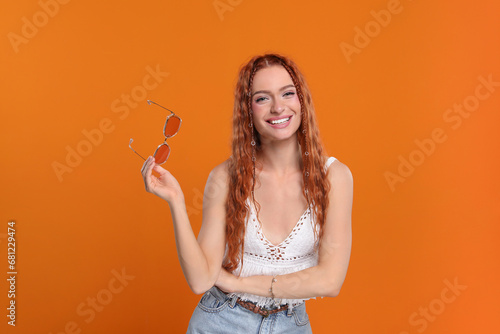 Stylish young hippie woman with sunglasses on orange background