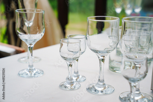 Empty wine glasses and shot glasses on a table with a white tablecloth.