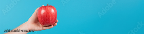 A woman's hand delicately holds a vibrant red apple, a symbol of freshness and healthy living, Banner, place for text.