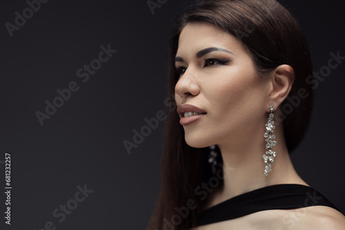 Side profile of a graceful woman in an elegant black outfit  her gaze directed away  and adorned with sparkling statement earrings