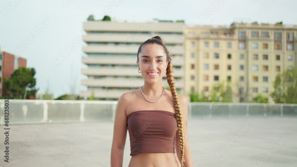 Smiling female in stylish outfit with long braid. Portrait of smiling young woman in stylish clothes with long braided hair looking at camera while standing against cityscape Smiling female in stylish outfit with long braid. Portrait of smiling young woman in stylish clothes with long braided hair looking at camera while standing against cityscape