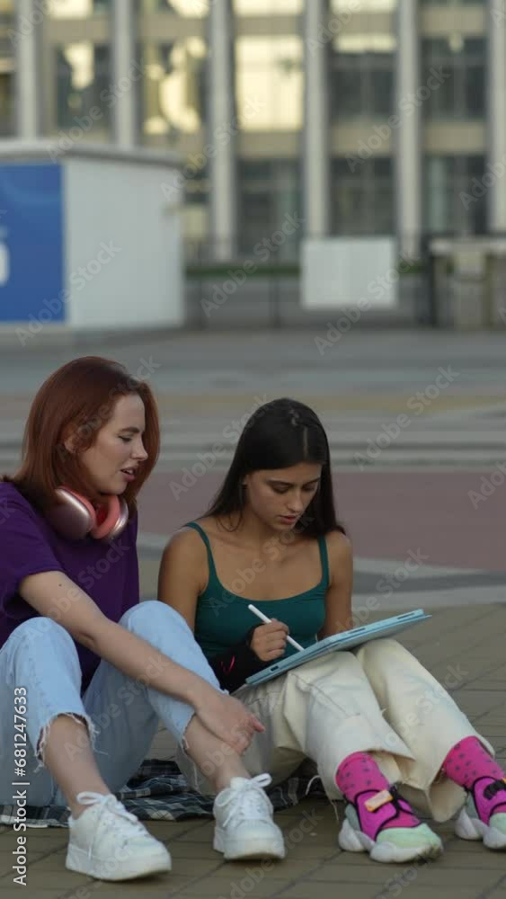 Two friends seated in the middle of the street, working with a tablet on a sunny day.