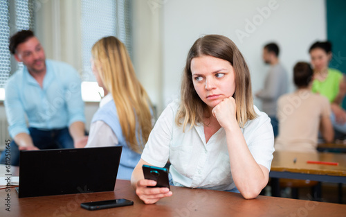 Female university student sitting at table in class room during recess and using smartphone.