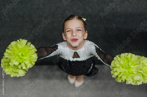 Принти на полотні Smiling happy girl athlete cheerleader in a suit with pompoms, an 8-year-old child with makeup, face painting, a champion rejoices at victory at a cheerleading competition