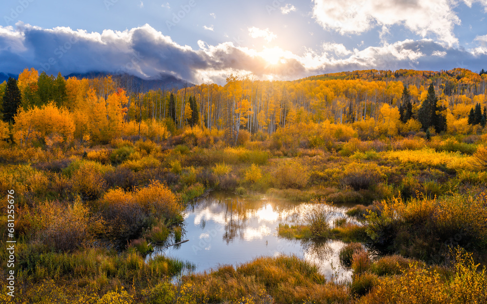 Heaven on earth outdoor Autumn scene of yellow Aspen trees and reflective pond with warm sunlight lens flare.