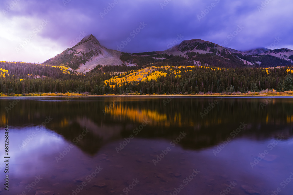 Beautiful purple Sunrise over reflective mirror Lost Lake Colorado in Autumn with yellow Aspen trees and snow covered mountains. 