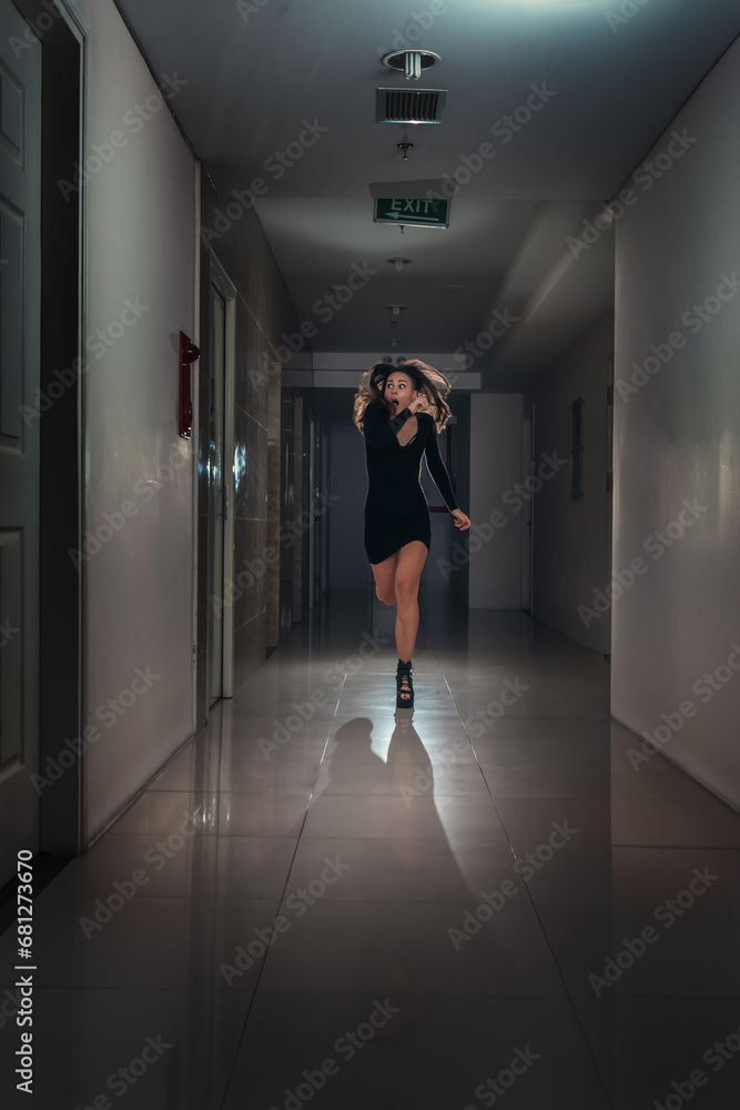 A young scared woman in a panic runs away along a dark corridor.