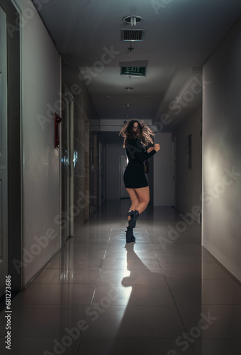 A young scared woman in a panic runs away along a dark corridor.
