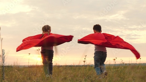 Kids donning superhero capes frolic and run across open field at evening sunset