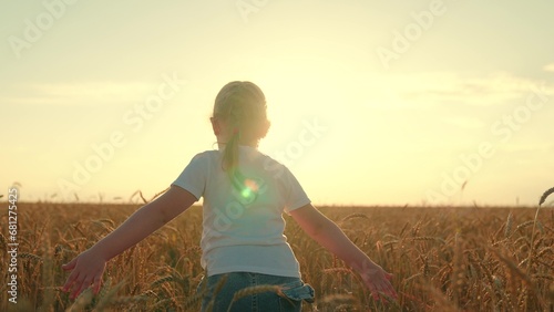Child girl run across wheat field, sunset. Little girl runs on wheat field, wants to be superhero. Child dreams of flying, family is on walk. Happy little girl running. Child girl plays dream at sun