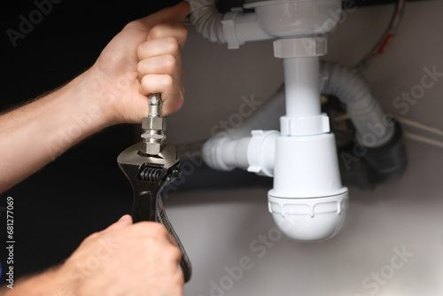 Professional plumber with adjustable wrench fixing sink indoors, closeup