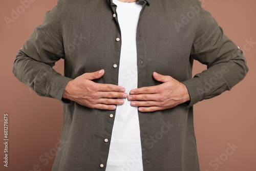 Man suffering from stomach pain on light brown background, closeup