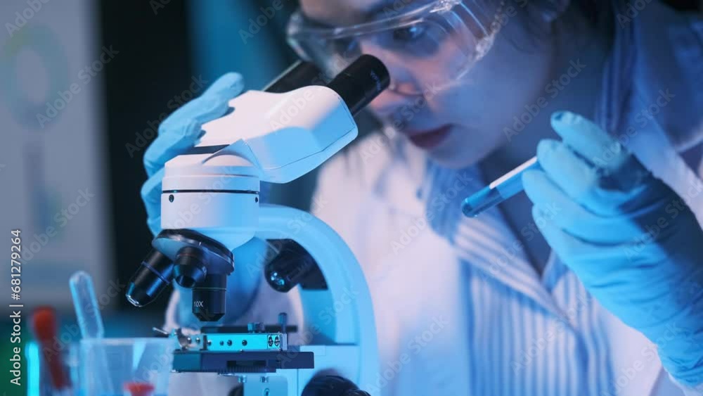 Young scientists conducting research investigations in a medical laboratory, a researcher in the foreground is using a microscope Young scientists conducting research investigations in a medical laboratory, a researcher in the foreground is using a microscope