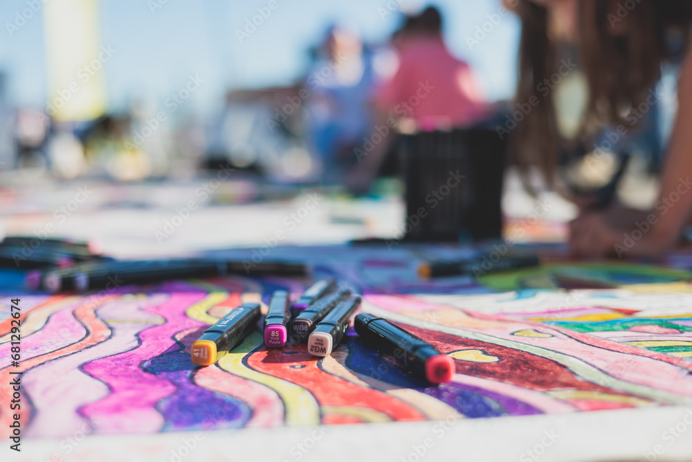 Fototapeta premium Proces rysowania na asfalcie i chodniku, dzieci i młodzież z kredkami, kredą i markerami, nastolatkowie tworzący sztukę uliczną na ziemi, graffiti i obrazy na bokach, festiwal malarstwa ulicznego