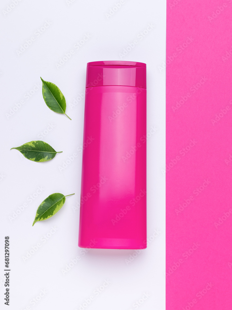 A bottle for shampoo or balm and green leaves on a two-tone background. A bottle for shampoo or balm and green leaves on a two-tone background.