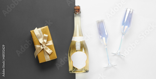 Bottle of champagne, glasses and Christmas gift on black and white backgrounds