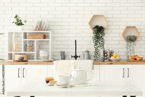 Interior of light kitchen with teapot, cup and snacks on table photo