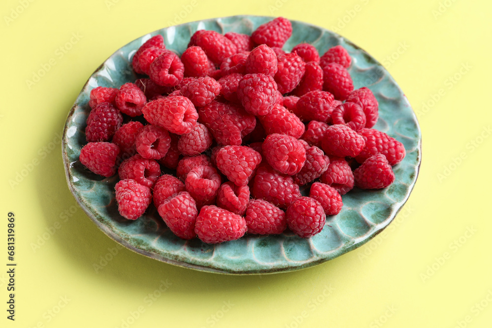Plate with fresh raspberries on yellow background Plate with fresh raspberries on yellow background