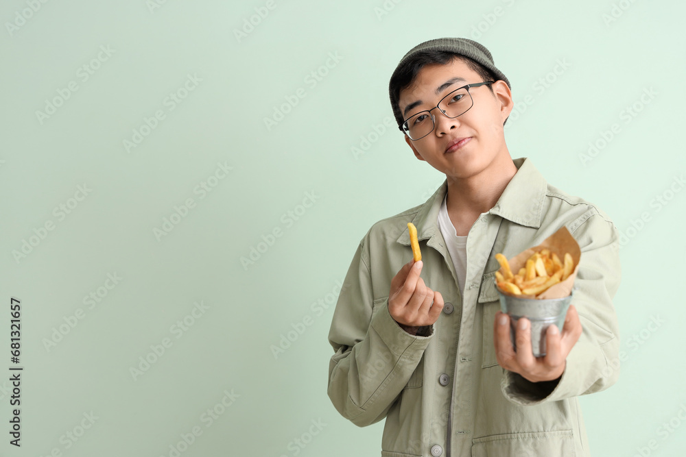 Young Asian man with bucket of french fries on green background Young Asian man with bucket of french fries on green background