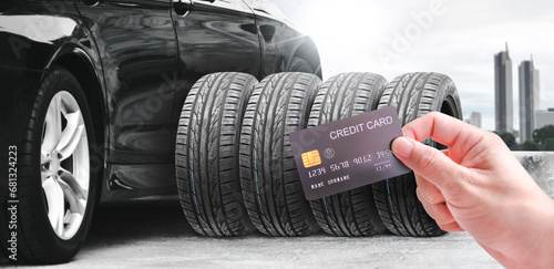 Hand holding a credit card with a row of tires and a black car on the background , Concept of car maintenance and credit card payments photo