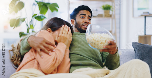 Fear, jump and couple watching tv on a sofa with popcorn for movie, film or streaming show at home. Omg, television and people hug in living room with cinema snack for scary, horror or spooky series