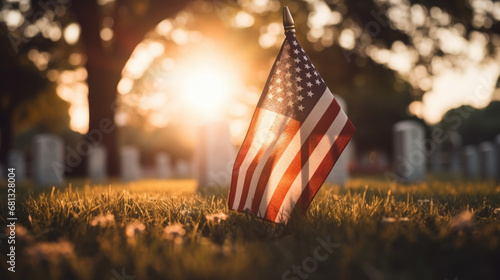 flag on the grass, American national flag with stars and stripes placed on green grass near tombstone in cemetery against bright sunset light and blurred  photo