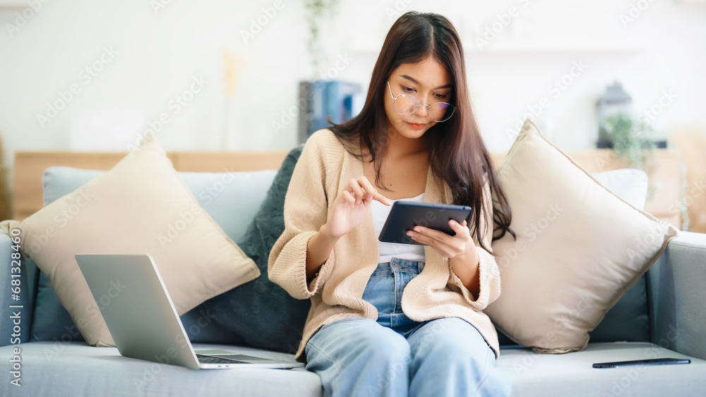 Young asian woman wearing glasses and using tablet while seated on couch at home Young asian woman wearing glasses and using tablet while seated on couch at home