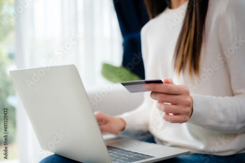 Young asian woman sitting on sofa in living room  makes online banking payments through the internet from bank card on computer laptop. Shopping online on notebook with credit card