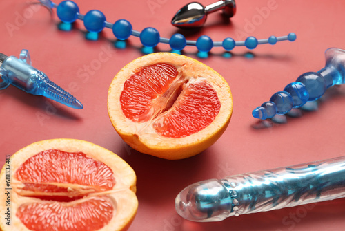 Different sex toys and tasty grapefruit on red background, closeup