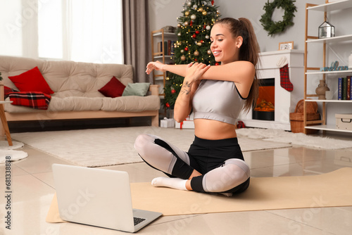 Sporty young woman with laptop training at home on Christmas eve photo
