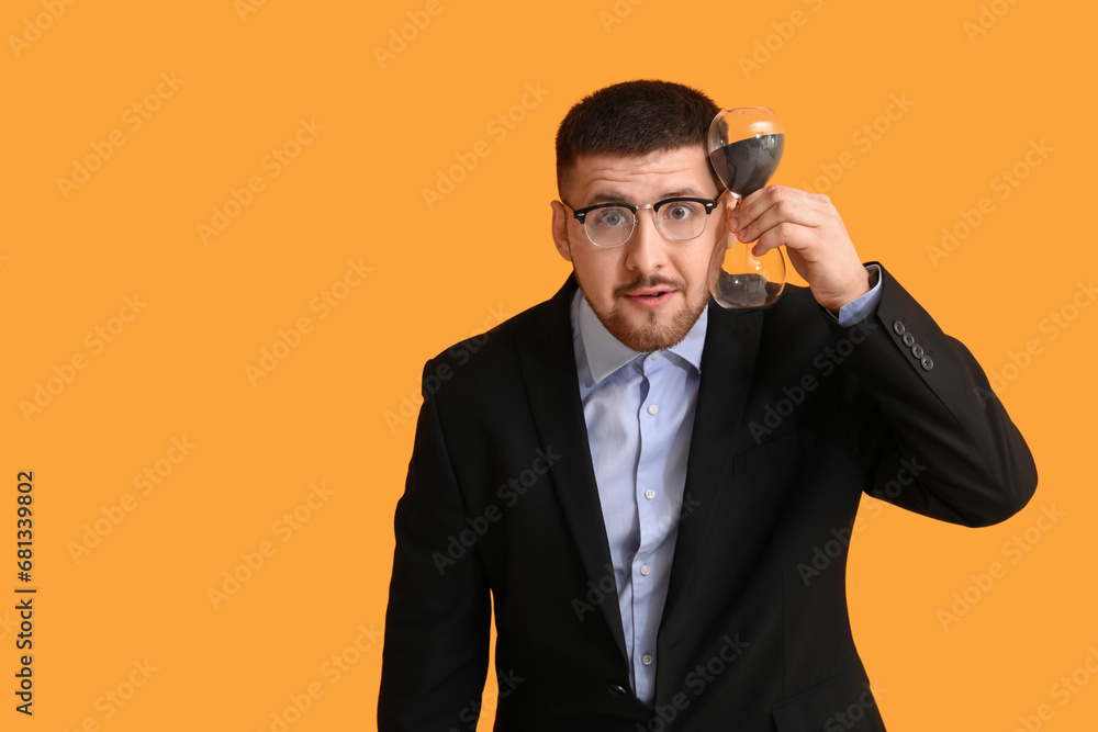 Young businessman with hourglass on yellow background. Time management concept Young businessman with hourglass on yellow background. Time management concept