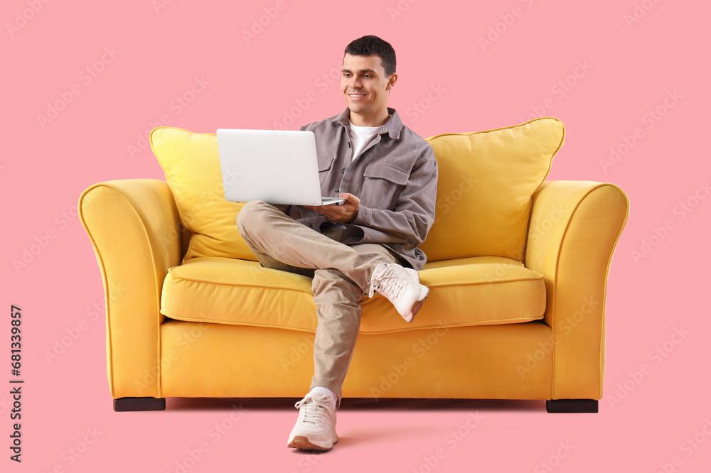 Young man using laptop on sofa against pink background