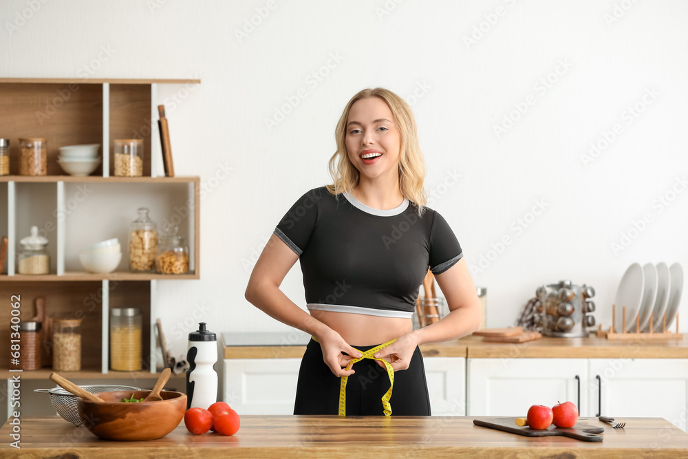 Beautiful sporty woman measuring her waist in kitchen at home. Weight loss concept Beautiful sporty woman measuring her waist in kitchen at home. Weight loss concept