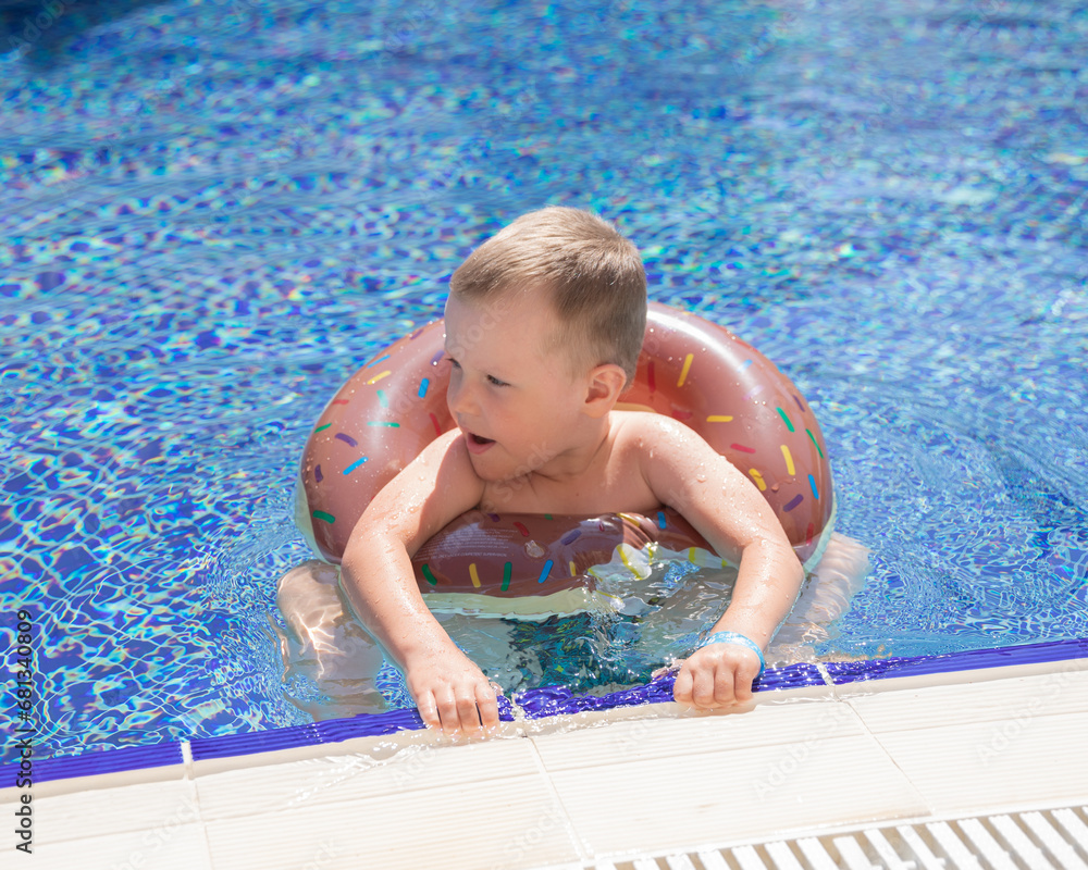 Little boy bathing in swimming pool with lifebuoy donut, smiling and happy