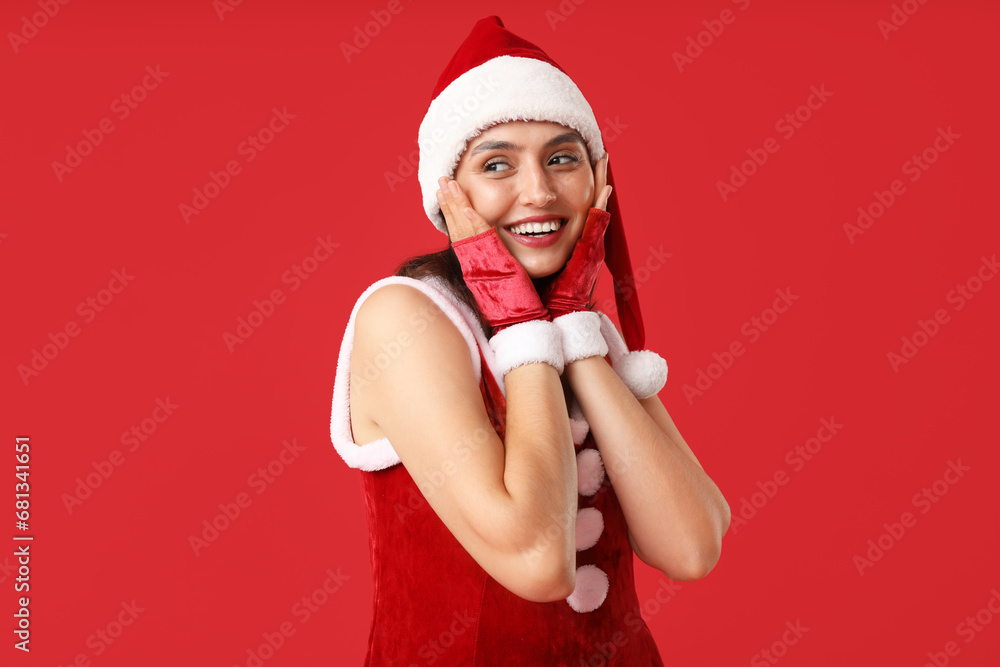 Happy young woman in Santa Claus costume on red background Happy young woman in Santa Claus costume on red background