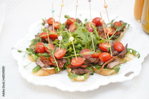 Mini sandwiches with tomatoes and slices of meat are laid out on a plate.