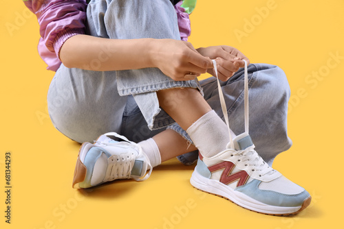 Woman in stylish sneakers sitting on color background, closeup