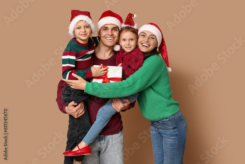 Happy family in Santa hats with Christmas gift on beige background