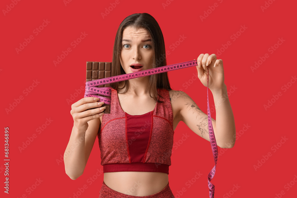 Young woman with chocolate bar and tape measure on red background