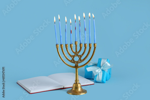 Menorah with burning candles, Torah and gifts for Hanukkah celebration on color background