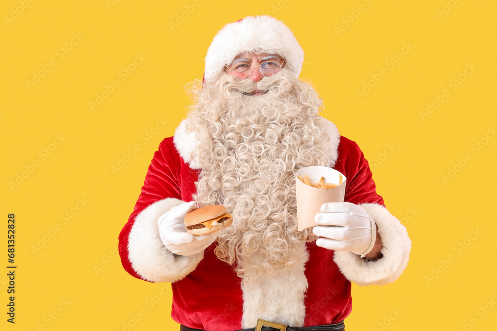 Santa Claus with tasty burger and french fries on yellow background Santa Claus with tasty burger and french fries on yellow background