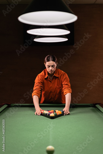 Young brazilian woman placing colorful pyramid of billiard balls in billiard triangle on green pool table photo