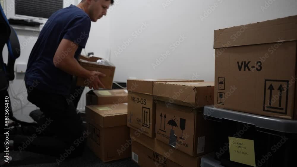 A young man stacks cardboard boxes in a room ready for the move and nods happily. A young man stacks cardboard boxes in a room ready for the move and nods happily.