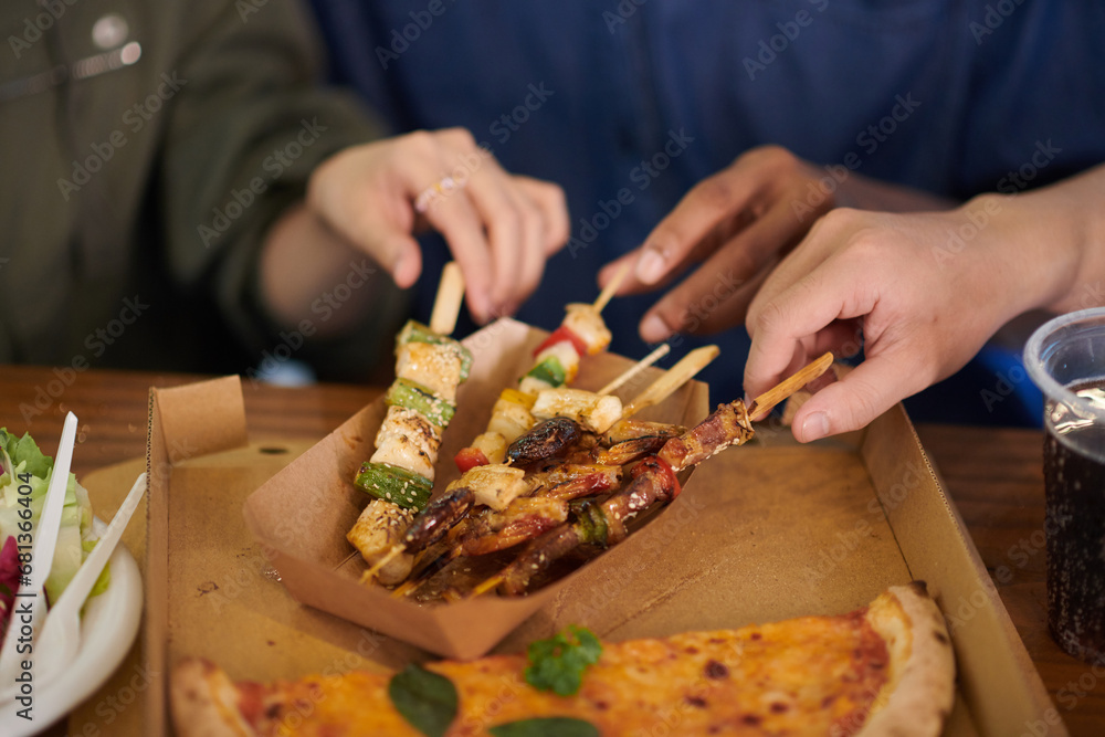 Hands taking wooden skewers with meat and veggies from box