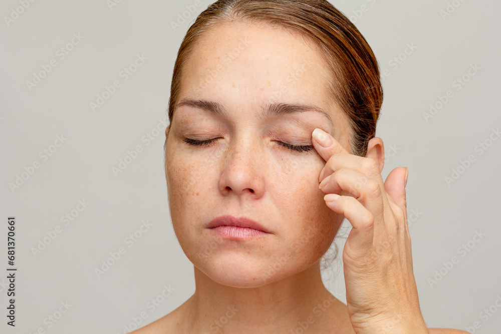 Middle aged caucasian woman of 40s with closed eyes holding finger on eyelid to show eyes aging - obrazy, fototapety, plakaty 