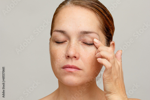 Middle aged caucasian woman of 40s with closed eyes holding finger on eyelid to show eyes aging photo